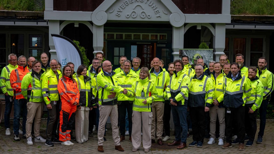 En stor gruppe mennesker i gule refleksjakker står samlet foran en bygning.